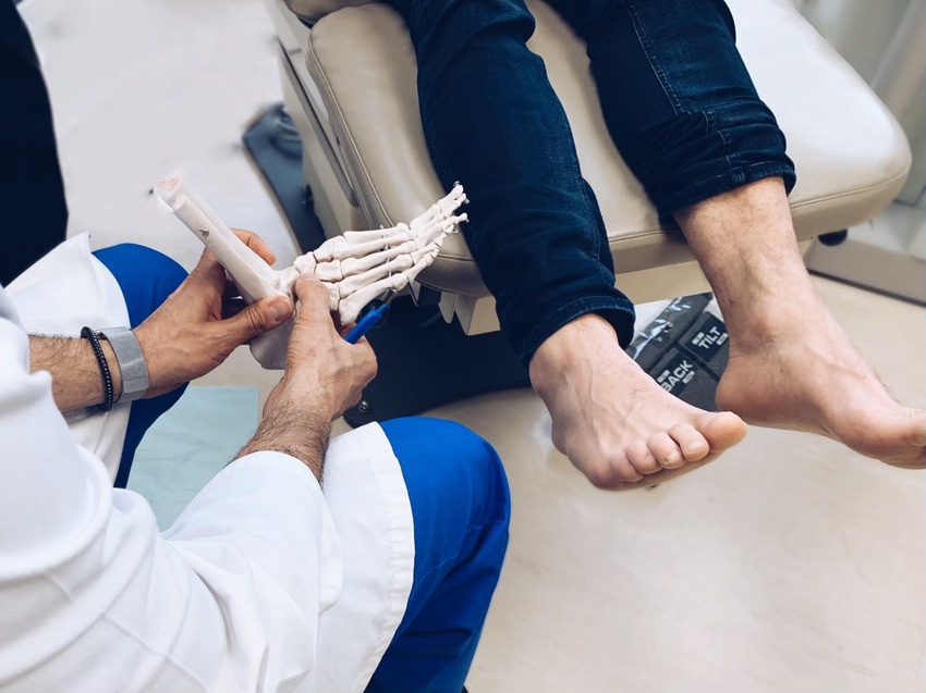 Docteur, de dos, qui tient un squelette de pied et qui parle à un patient